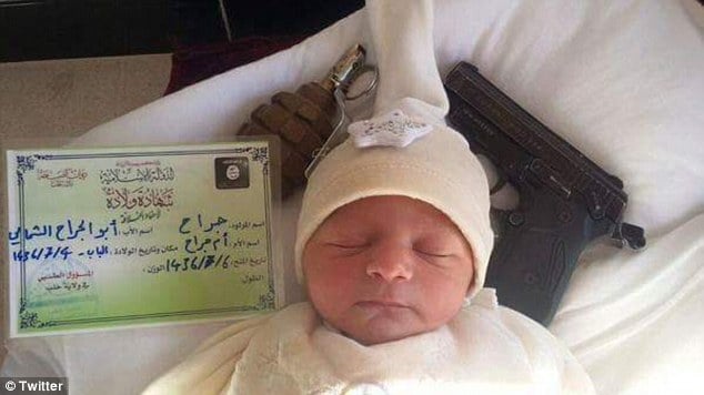 baby sleeping beside handgun and grenade underneath ISIS blanket