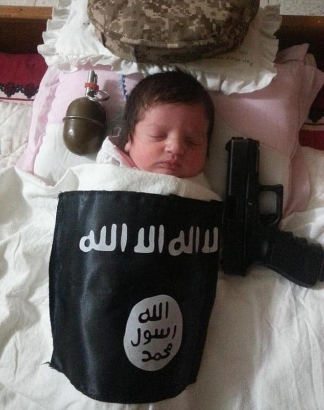 baby sleeping beside handgun and grenade underneath ISIS blanket